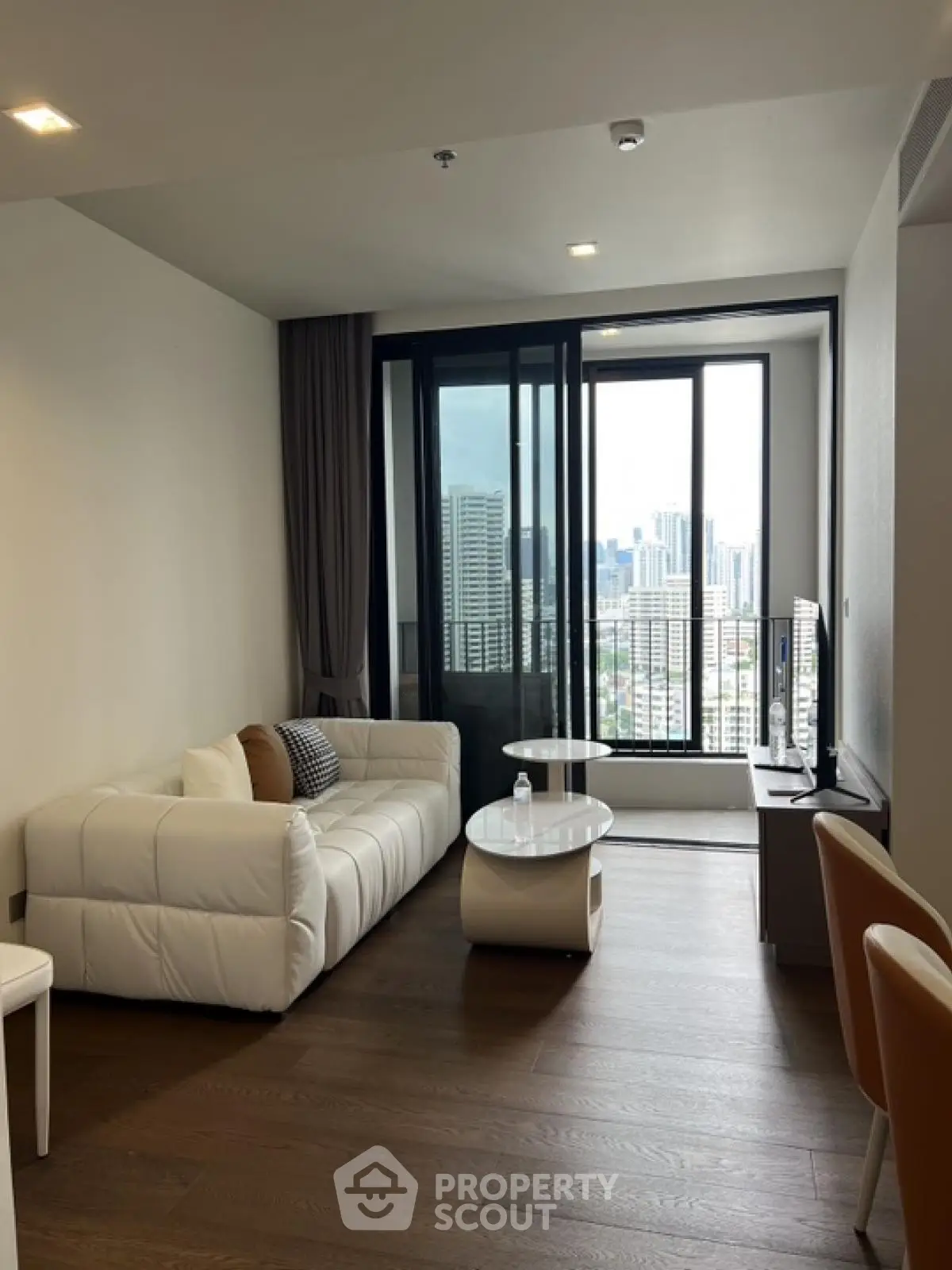 Modern living room with city view, featuring sleek furniture and floor-to-ceiling windows.