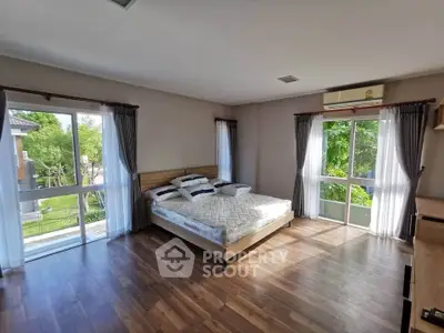 Spacious bedroom with large windows and garden view, featuring wooden flooring and modern decor.