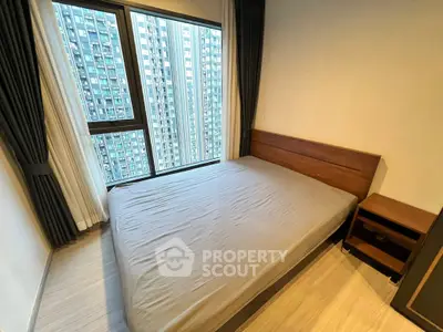 Modern bedroom with large window and city view in high-rise apartment.