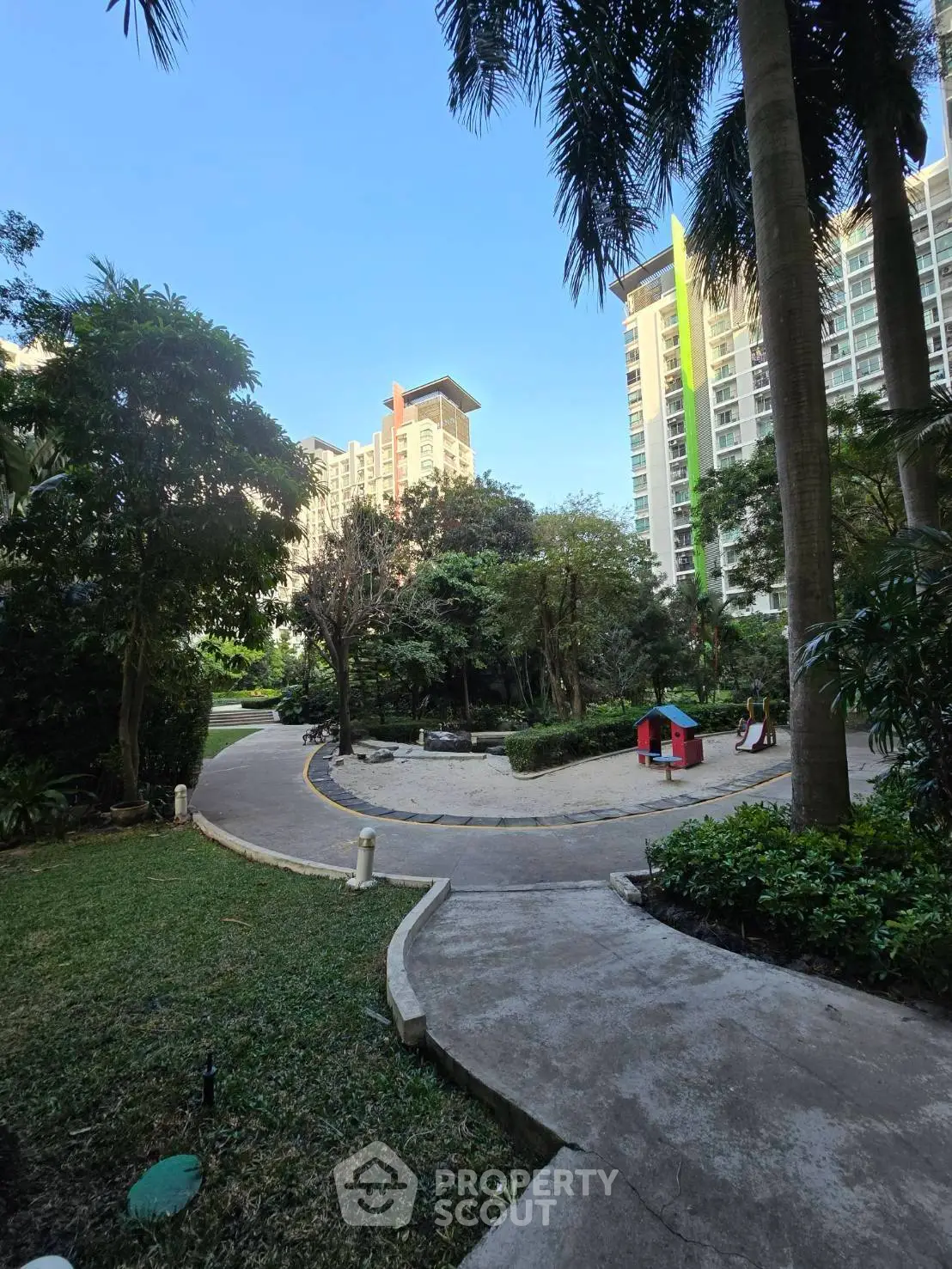 Lush garden pathway in modern residential complex with high-rise buildings and play area.