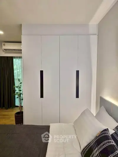 Modern bedroom with sleek white wardrobe and cozy bedding, featuring natural light and stylish decor.