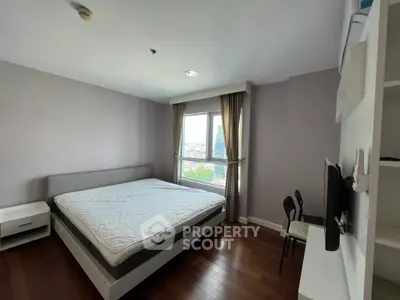 Spacious bedroom with large window offering city view, featuring modern furniture and wooden flooring.