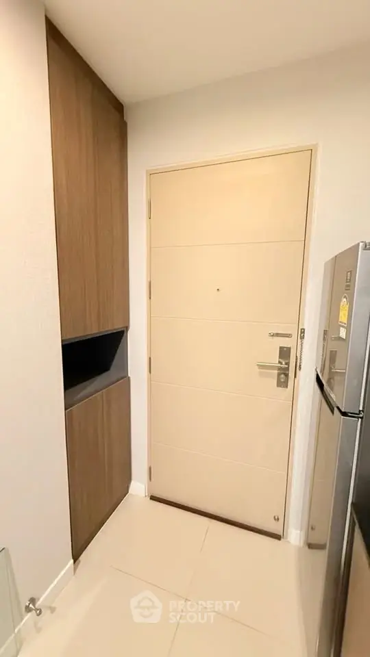 Modern apartment entrance with sleek wooden cabinetry and stainless steel fridge