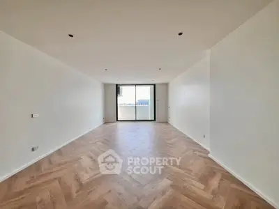 Spacious empty living room with wooden flooring and large window view.