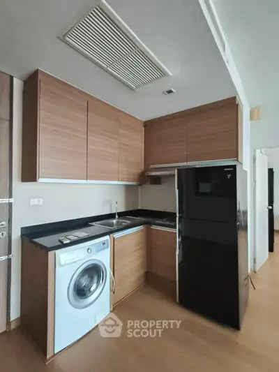 Modern kitchen with sleek wooden cabinets, black countertops, and built-in appliances including a washing machine.