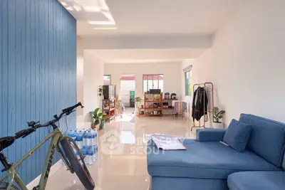 Spacious living room with modern decor and natural light, featuring a cozy blue sofa and stylish shelving.