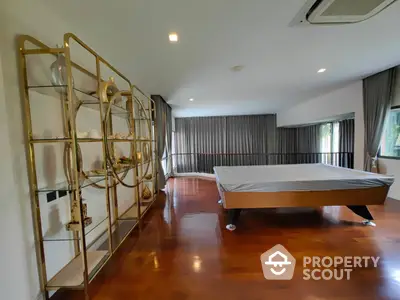 Spacious bedroom with polished wooden floors, large bed, and elegant gold-accented shelving unit, surrounded by full-length drapery.