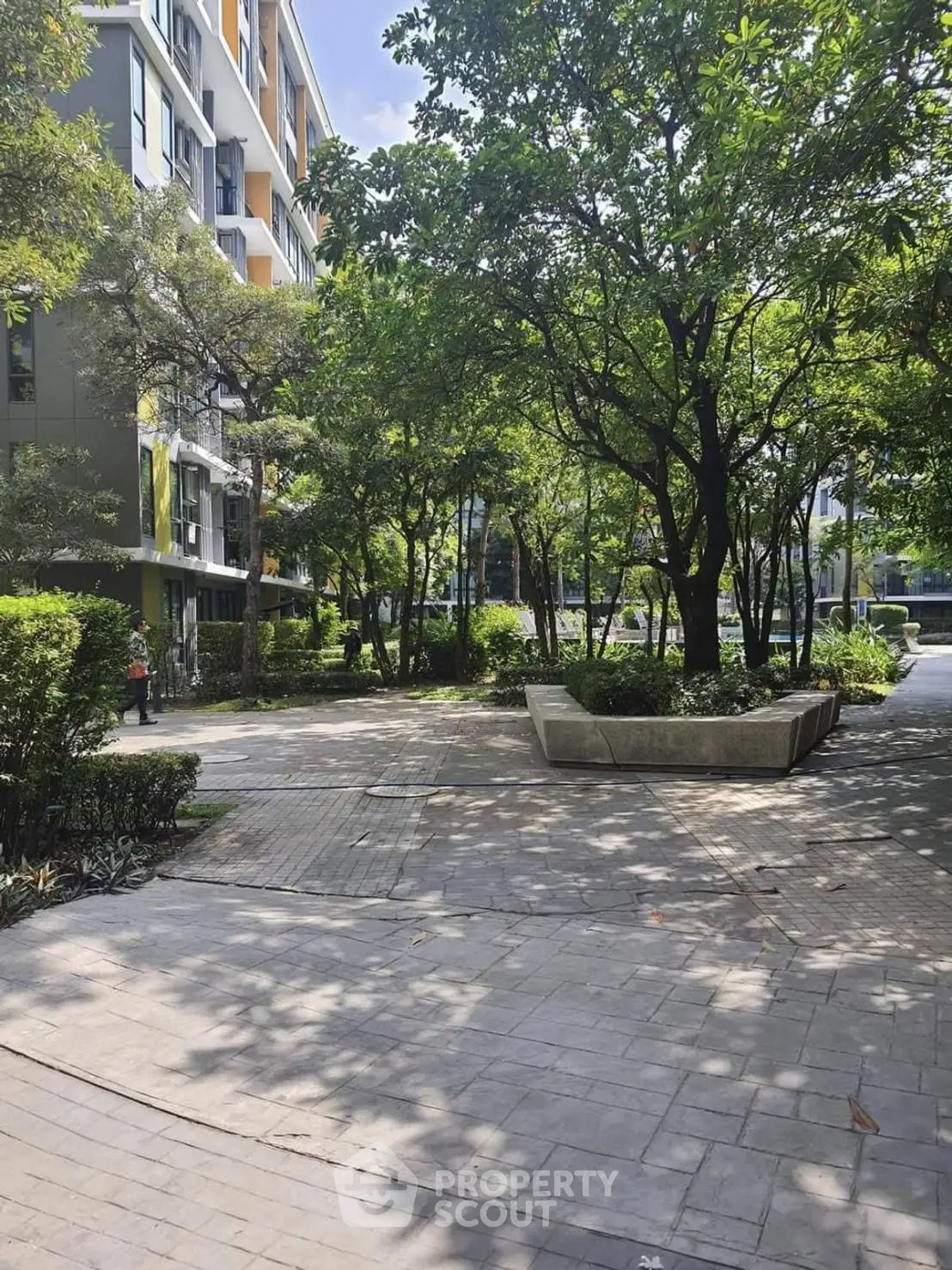 Lush garden area in modern residential complex with paved pathways and mature trees.