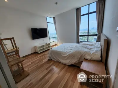 Modern bedroom with large windows and city view, featuring wooden flooring and minimalist furniture.