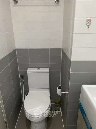 Modern bathroom with sleek gray and white tiles, featuring a compact toilet and sink.