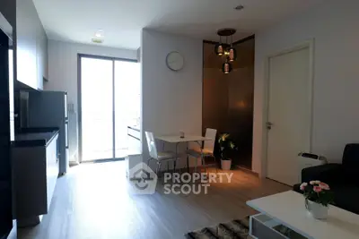 Modern living room with open kitchen, stylish lighting, and natural light from large window.