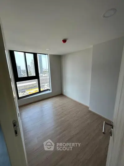 Bright empty room with large window and wooden flooring, ideal for customization.