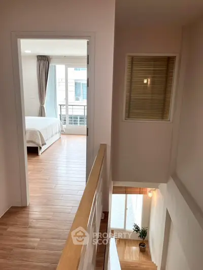 Bright hallway leading to a cozy bedroom with wooden flooring and large window.