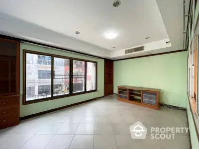 Spacious living room with large windows allowing ample natural light, featuring elegant tile flooring and built-in wooden cabinetry.