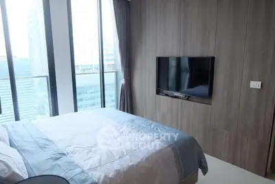 Modern bedroom with large windows and city view, featuring a wall-mounted TV.