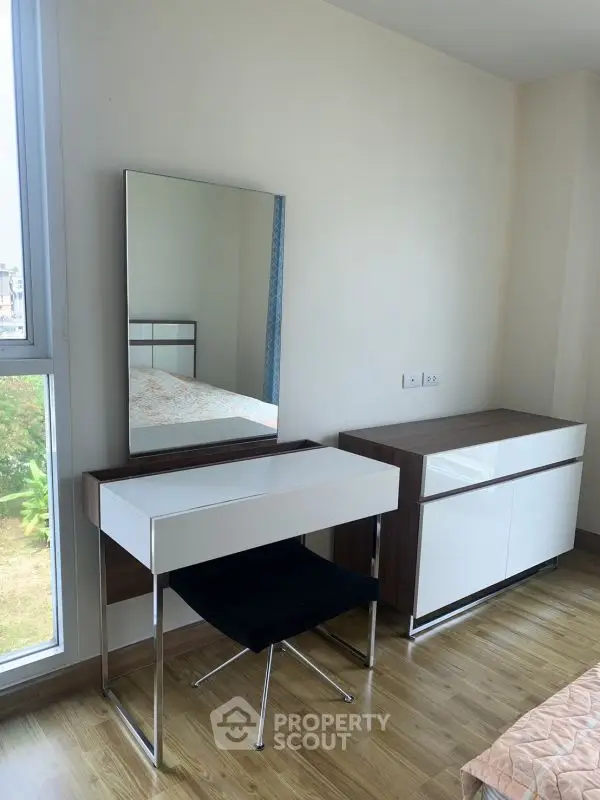 Modern bedroom with sleek vanity and large window offering natural light.