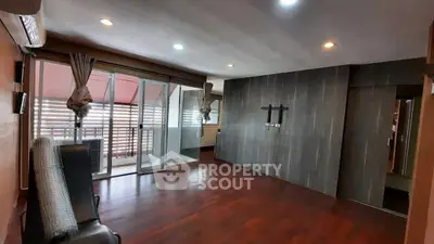 Spacious living room with wooden flooring and large windows opening to a balcony.