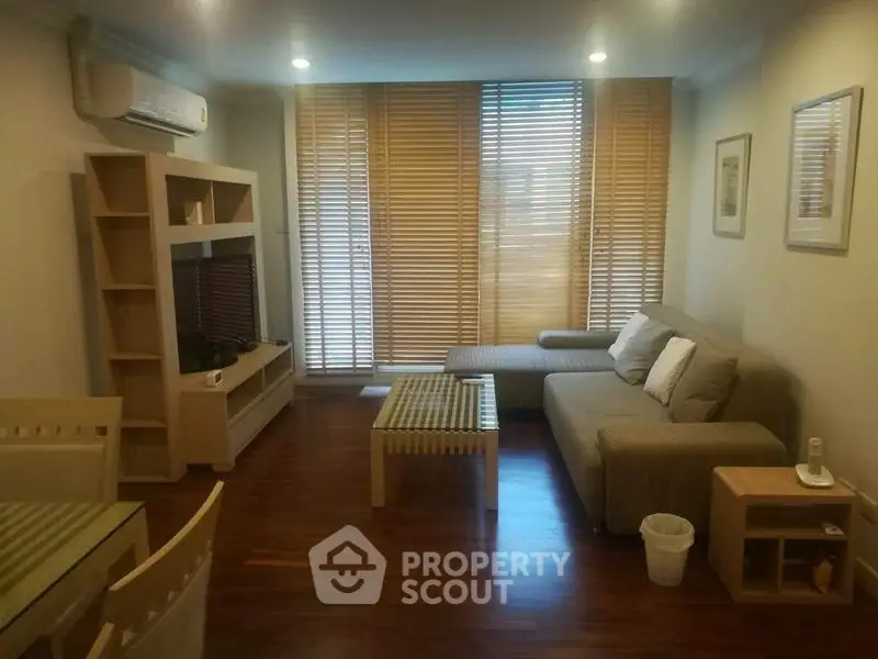 Cozy living room with modern furniture and wooden flooring, featuring a comfortable sofa and stylish blinds.