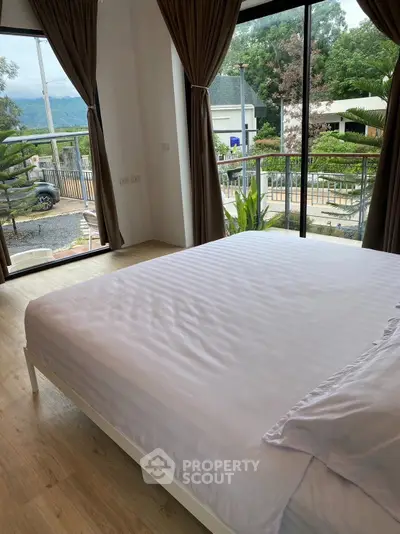Spacious bedroom with large windows offering a scenic view and natural light, perfect for relaxation.
