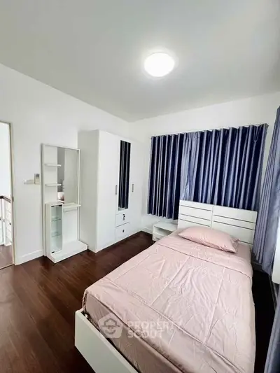 Modern bedroom with wooden flooring, stylish bed, and ample natural light through large windows.