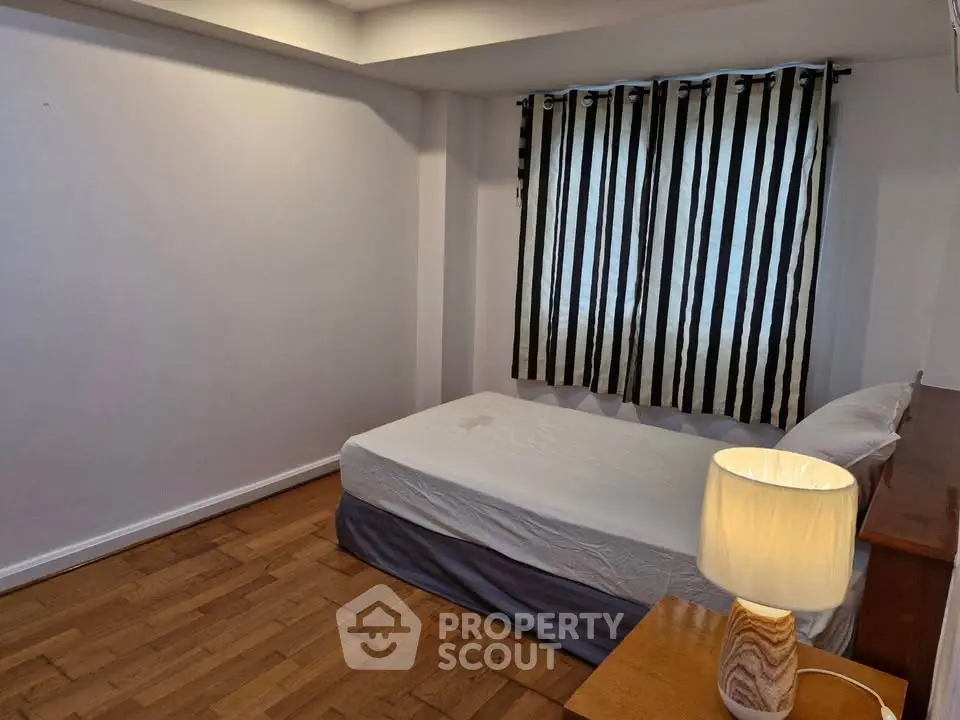 Cozy bedroom with wooden flooring and striped curtains, featuring a comfortable bed and a stylish lamp.