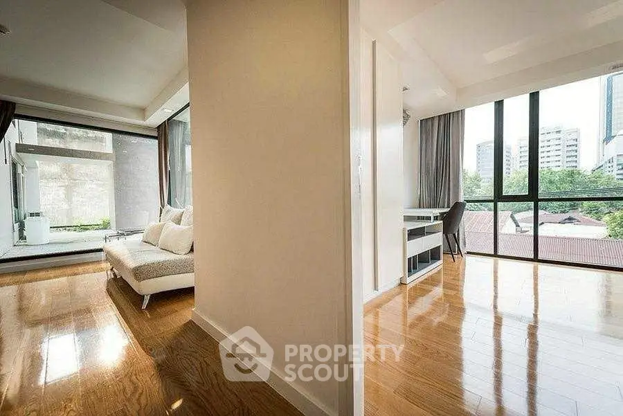 Spacious modern apartment with hardwood floors and large windows offering city views.