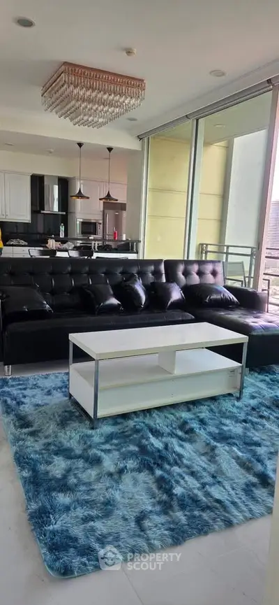 Modern living room with sleek black sofa, chic chandelier, and open kitchen layout.