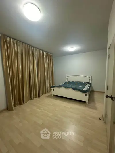 Spacious bedroom with wooden flooring and elegant curtains, featuring a cozy bed.