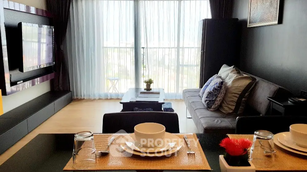 Modern living room with large TV, cozy sofa, and dining area with elegant table setting.