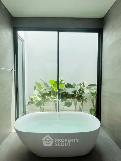 Luxurious bathroom with modern freestanding bathtub and lush greenery view.