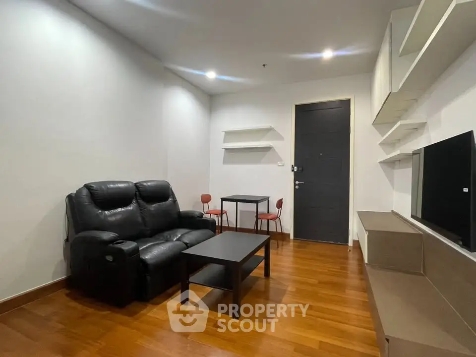 Modern living room with sleek black leather sofa, wooden flooring, and minimalist decor.