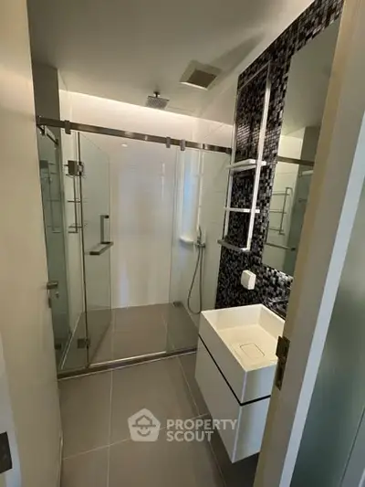Modern bathroom with glass shower enclosure and sleek vanity in contemporary apartment.