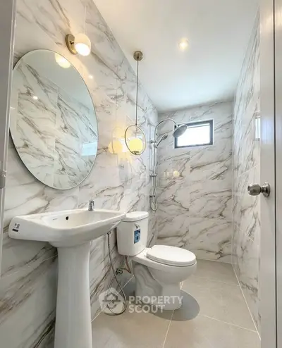 Modern bathroom with marble tiles, round mirror, and elegant fixtures.