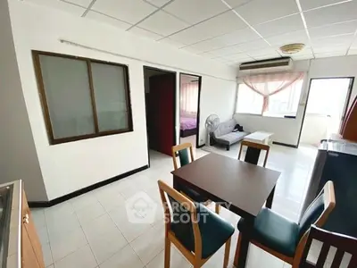 Spacious apartment with open dining area and natural light, featuring modern furniture and tiled flooring.