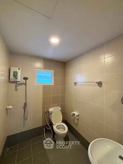 Modern bathroom with shower and toilet in minimalist design, featuring neutral tiles and bright lighting.