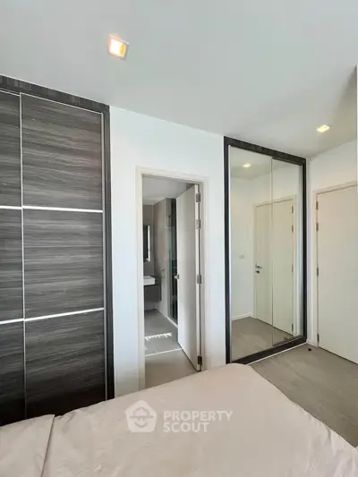 Modern bedroom with mirrored closet and ensuite bathroom in stylish apartment.