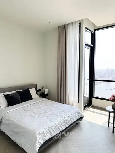 Modern bedroom with large windows offering stunning city and water views, featuring elegant decor and natural light.
