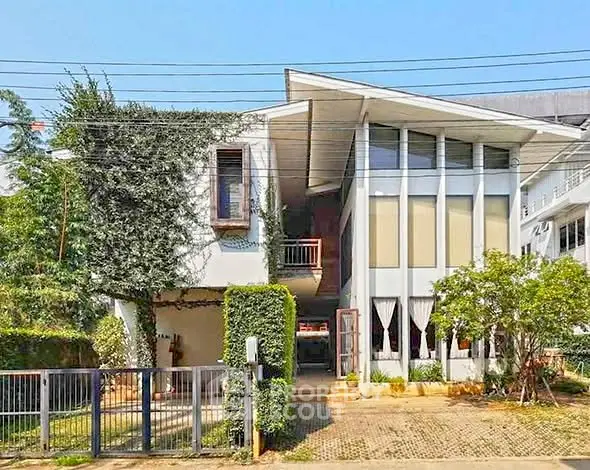 Modern two-story house with large windows and lush greenery in a serene neighborhood.