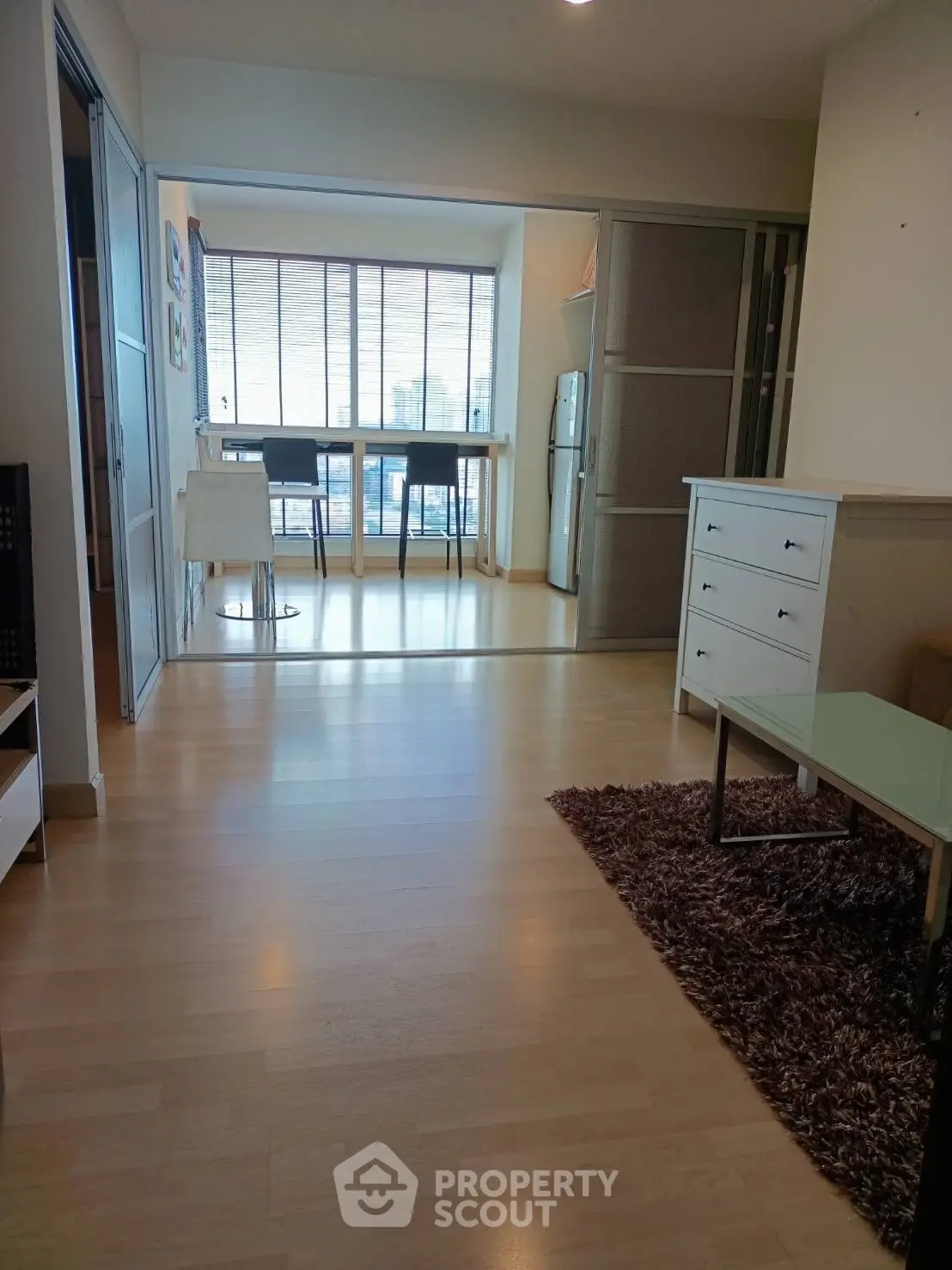 Spacious modern living room with wooden flooring and large windows offering city views.