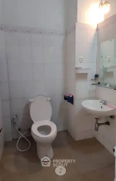 Compact bathroom with white tiles, toilet, sink, and mirror, ideal for small apartments.