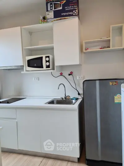 Modern kitchen with sleek white cabinets, microwave, and stainless steel fridge in cozy apartment.