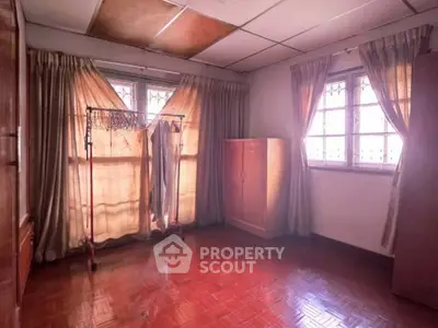 Spacious room with wooden flooring and ample natural light, featuring a wardrobe and clothing rack.