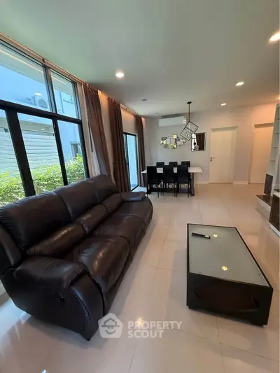 Spacious modern living room with leather sofa and dining area, featuring large windows and elegant decor.
