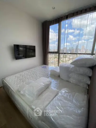 Modern bedroom with city view, featuring a wall-mounted TV and large windows for natural light.