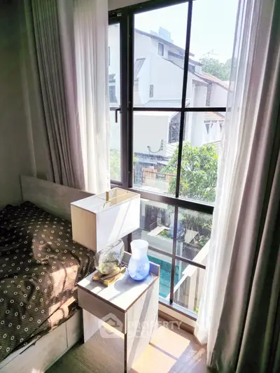 Cozy bedroom corner with a large window offering abundant natural light and a serene view, complemented by sheer curtains and modern decor.