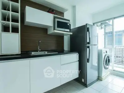 Modern kitchen with sleek cabinetry, stainless steel fridge, and washing machine in bright apartment.
