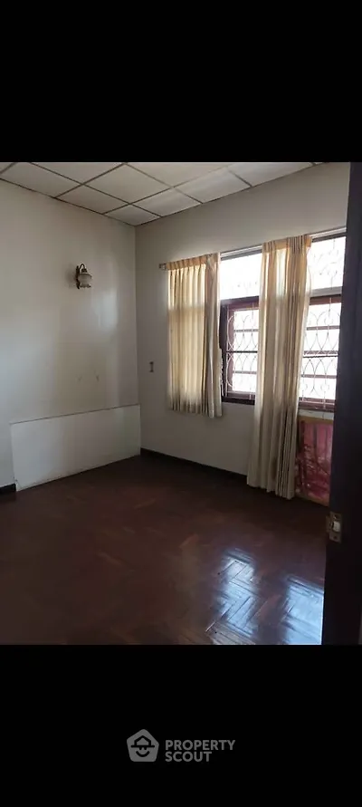 Spacious empty room with wooden flooring and natural light from large windows.