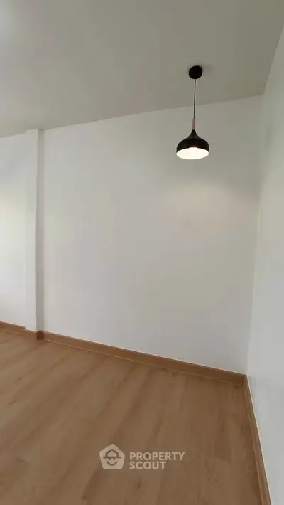 Minimalist interior with wooden flooring and modern pendant light, perfect for versatile living space.