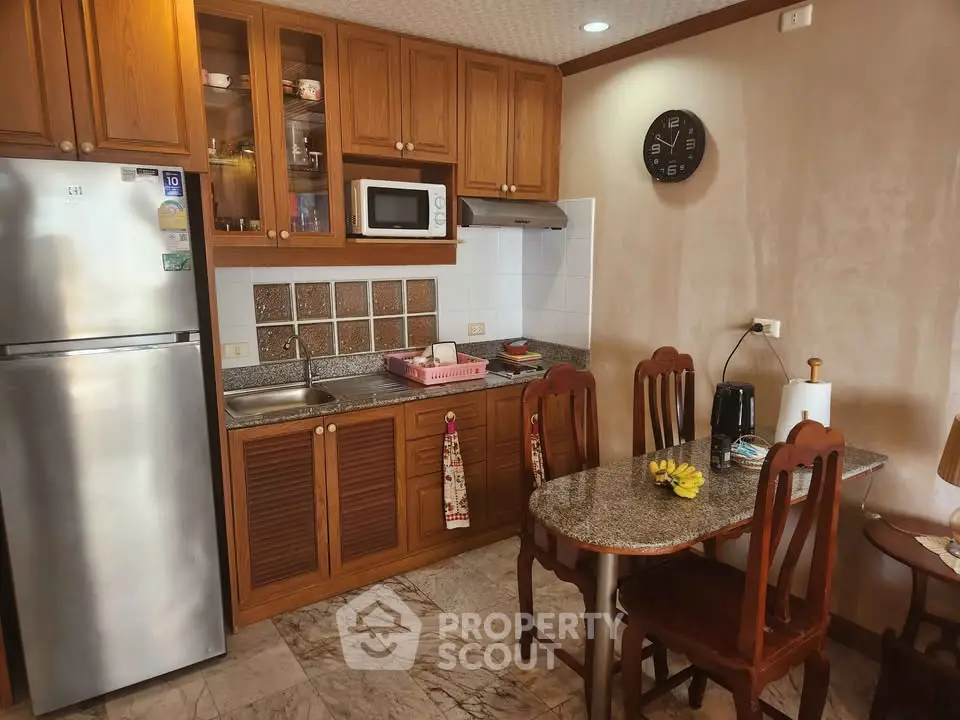 Charming kitchen with wooden cabinets and dining area, featuring a stainless steel fridge and microwave.
