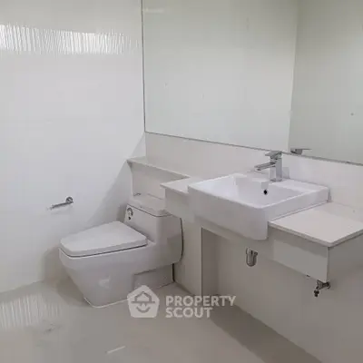 Modern minimalist bathroom with sleek white fixtures and large mirror.
